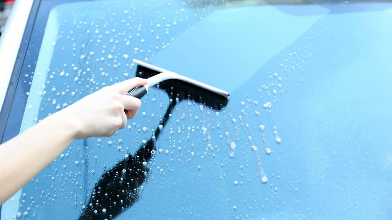 using a car blade to sweep soap off a car glass