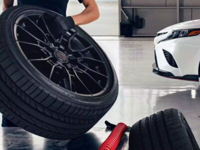 Technician holding a car tire with a white Camry in the background